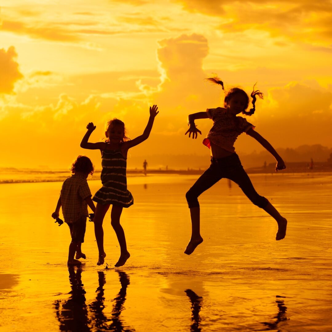 A group of people jumping in the air on top of a beach.