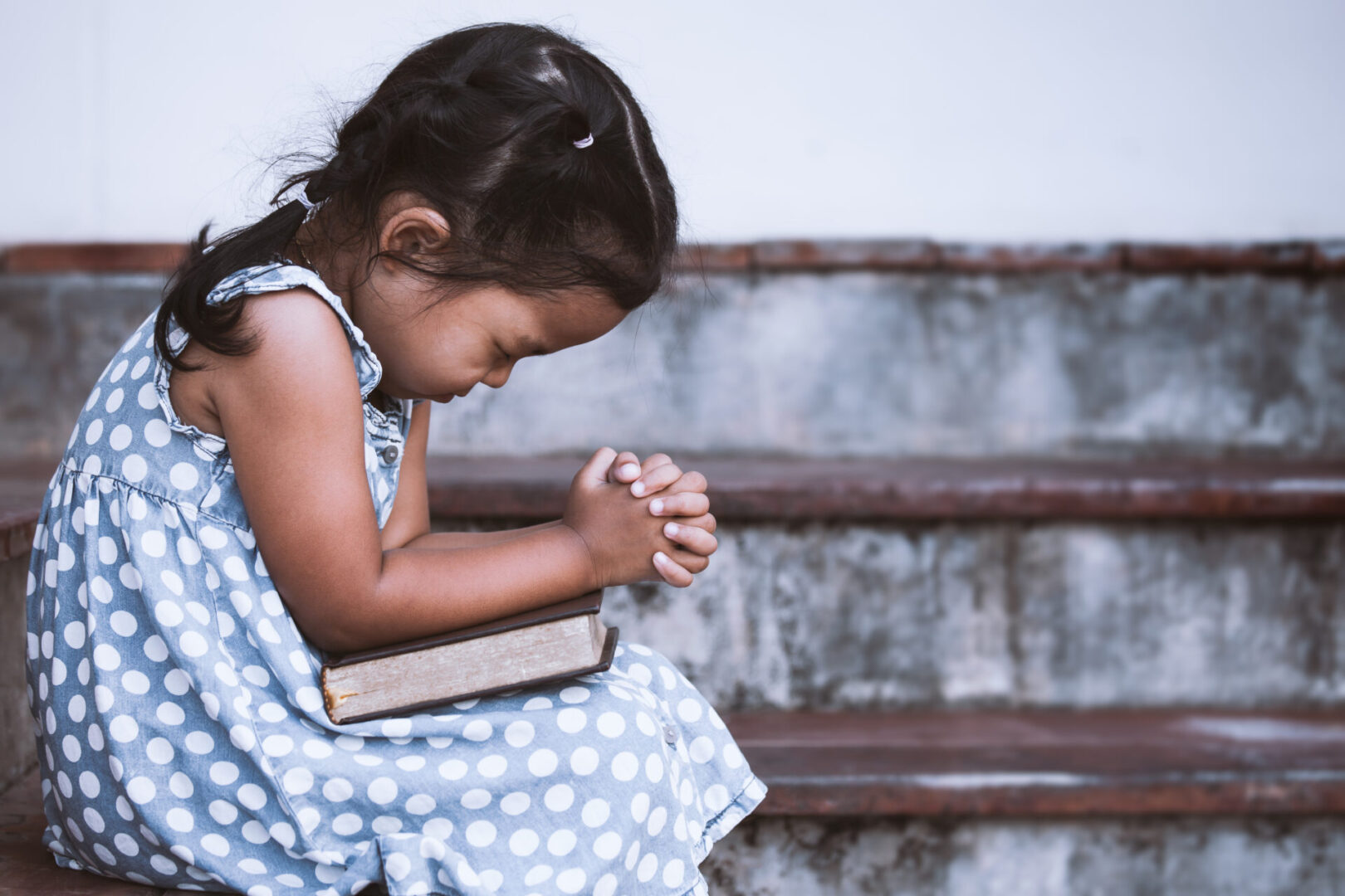 A little girl sitting on the steps holding a book.